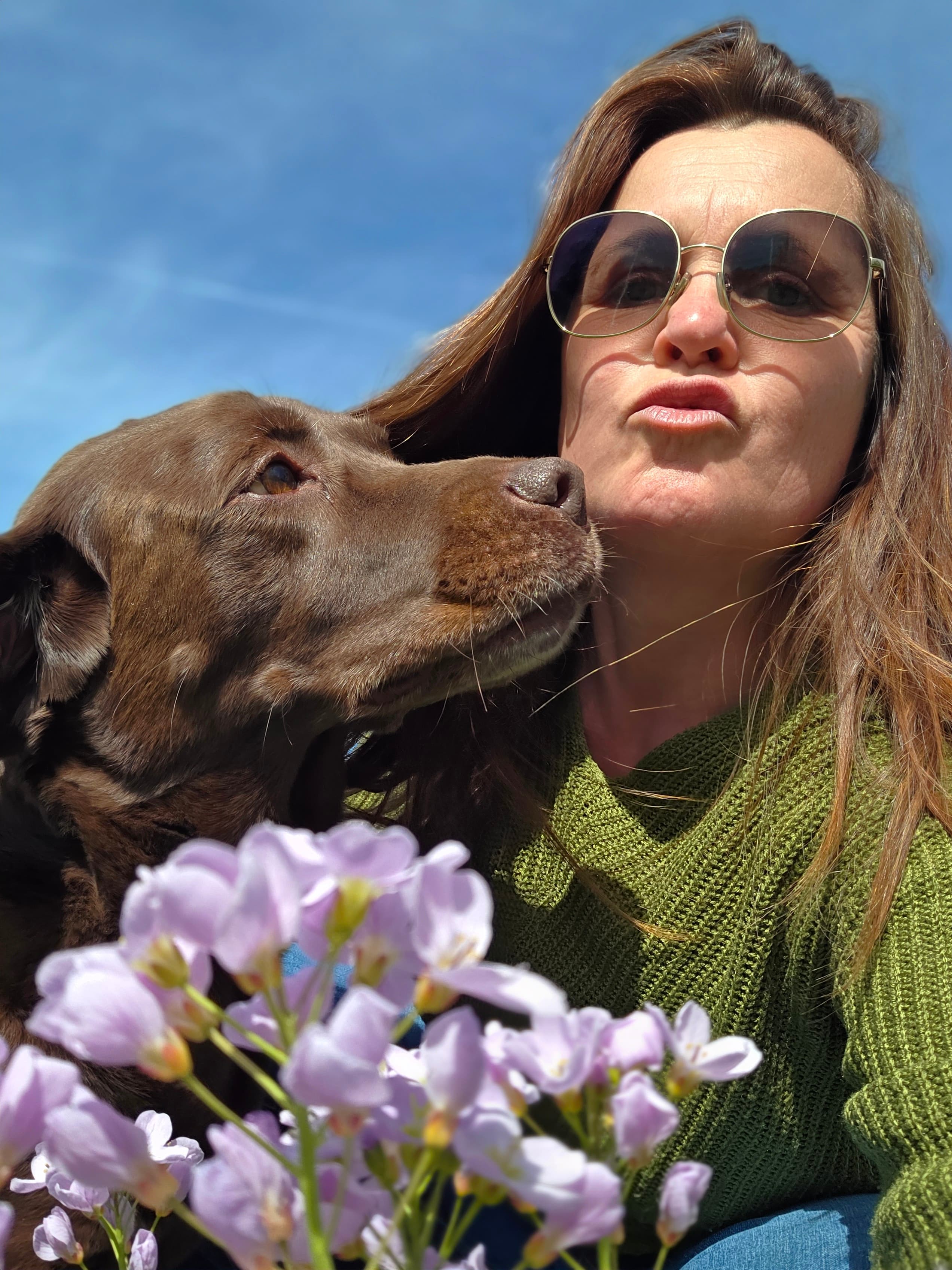 Raphaela Niewerth im Freien, dicht neben ihrem braunen Labrador, im Vordergrund blühende Wiesenblumen.