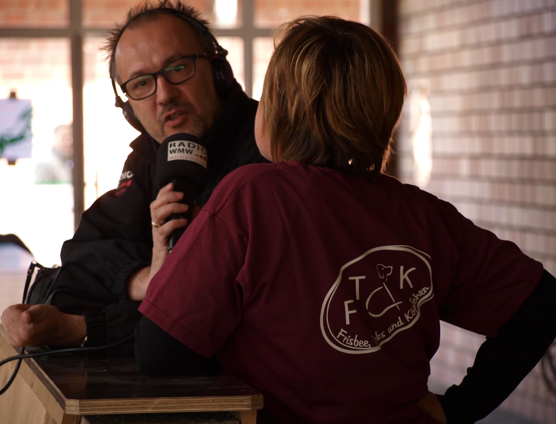 Eine Hundetrainerin im Vereins-Shirt spricht bei einer Veranstaltung in das Mikrofon eines Radioreporters.